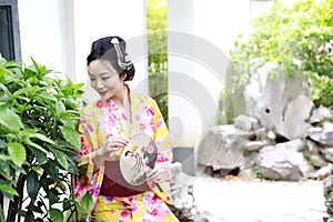 Traditional Asian Japanese beautiful woman wears kimono with fan on hand smiling playing on outdoor spring garden