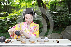 Traditional Asian Japanese beautiful woman wears kimono show tea art and ceremony sit on stone bench in outdoor spring garden