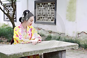Traditional Asian Japanese beautiful woman wears kimono sit on stone bench in outdoor spring garden