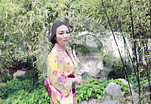 Traditional Asian Japanese beautiful woman wears kimono in a spring garden park stand by bamboo enjoy free time