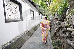 Traditional Asian Japanese beautiful woman wears kimono in a spring garden park stand by bamboo enjoy free time fan