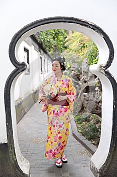 Traditional Asian Japanese beautiful woman wears kimono in a spring garden park stand by bamboo enjoy free time fan