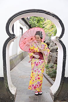 Traditional Asian Japanese beautiful woman wears kimono in a spring garden park stand by bamboo enjoy free time fan umbrella