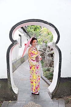 Traditional Asian Japanese beautiful woman wears kimono in a spring garden park stand by bamboo enjoy free time fan umbrella