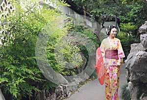 Traditional Asian Japanese woman bride Geisha wearing kimono play in a graden hold a red umbrella