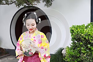 Traditional Asian Japanese woman Geisha wearing kimono hold a fan play in a graden