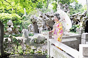 Traditional Asian Japanese woman Geisha wearing kimono play in a graden stand on a bridge hold a white umbrella