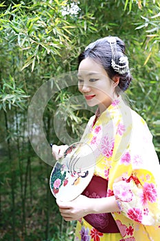 Traditional Asian Japanese woman with kimono with fan on hand stand by bamboo in a spring park