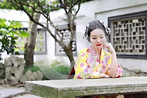 Traditional Asian Japanese woman in a outdoor garden sit on a stone bench