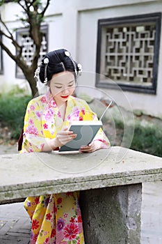 Traditional Asian Japanese woman reading a book sit on a stone bench in a garden