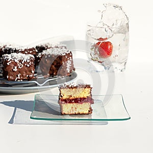 Traditional Australian lamington cakes with strawberry jam, chocolate and coconut. Against of a glass of water, a splash