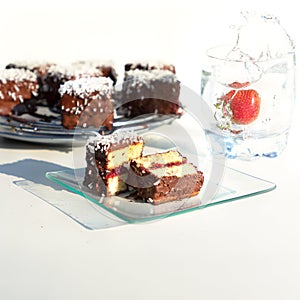 Traditional Australian lamington cakes with strawberry jam, chocolate and coconut. Against of a glass of water, a splash