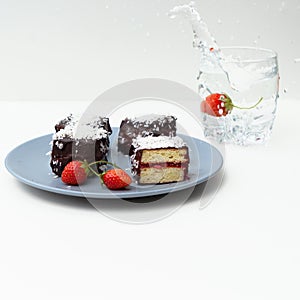 Traditional Australian lamington cakes with strawberry jam, chocolate and coconut. Against of a glass of water, a splash