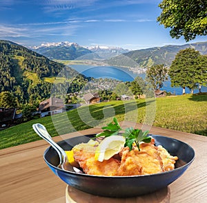 Traditional austrian food Wiener schnitzel against Zell am see village with lake in Austria