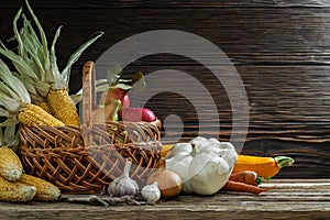 Traditional autumn set of ripe vegetables and fruits with a wicker basket on rough boards on a dark wooden background. artistic