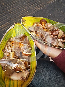 Traditional Babi Kecap or Braised Pork served in banana leaf and paper bowl