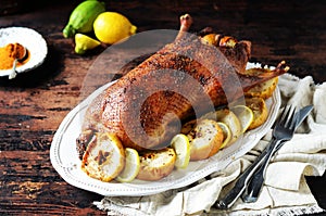 Traditional baked duck with apples and lemon on a dark wooden table