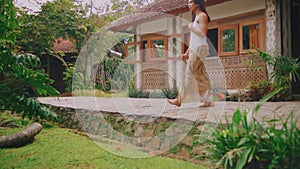 Traditional Balinese dancer performing in a tropical garden setting with a quaint villa backdrop