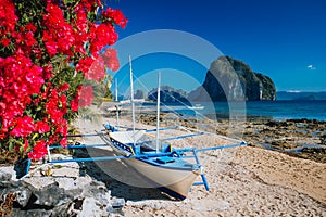 Traditional banca boat and vivid colored flowers at Las cabanas beach with amazing Pinagbuyutan island in background