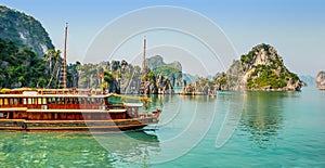 Traditional boat sailing in the green waters among the rock islands of Halong Bay Vietnam
