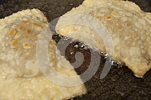 Traditional Brazilian food called PASTEL - Pastel in the frying pan in vegetable oil. Close-up. Top view