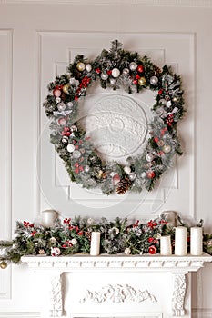 A traditional, bright Christmas wreath hanging over the fireplace, on a white wall. Christmas concept, new year.Interior