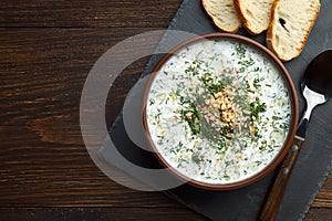 Traditional bulgarian chilled tarator in brown bowl with spoon and bread ready to eat.