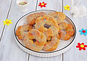 Traditional buttery twisted Italian Easter cookies with multicolored sugar decor on a white plate on a white wooden background.