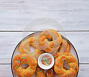 Traditional buttery twisted Italian Easter cookies with multicolored sugar decor on a white plate on a white wooden background.