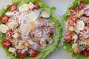 Traditional caesar salad in a white bowl on a old white table with leaves and a sauce boat and parmesan. Selected focus