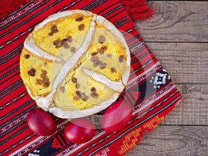 Traditional cheese and raisins pie and red easter eggs on a red cloth with an ethnic pattern