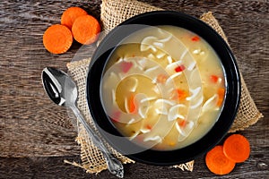 Traditional chicken noodle soup, overhead scene on rustic wood