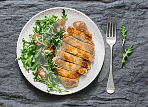Traditional chicken schnitzel with arugula cherry tomatoes salad on grey background