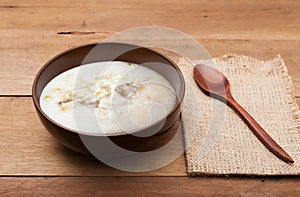 Traditional chinese porridge rice gruel in brown bowl with wooden spoon