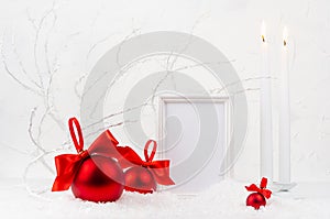 Traditional christmas background with blank photo frame mockup, burning candles, rich red glossy balls with satin ribbons, bows.