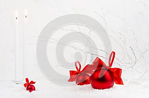 Traditional christmas background with white burning candles, rich red decorations - balls with satin ribbons, bows in white snow.