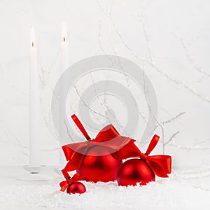 Traditional christmas background with white burning candles, rich red decorations - balls with satin ribbons, bows in white snow.