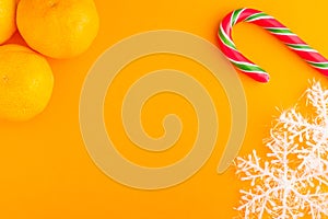 Traditional christmas caramel candy cane, mandarins and snowflakes on a orange background. Winter Holiday festive greeting card