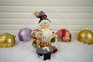 Christmas photography image of Santa Claus ornament sitting in snow with red and gold glitter tree decorations in background