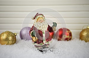 Christmas photography image of traditional Santa Claus ornament in snow with red and gold glitter tree decorations in background