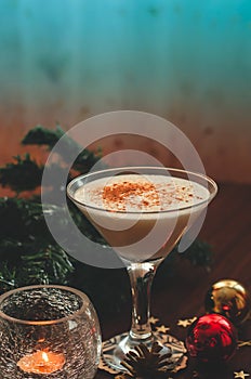 Traditional christmas eggnog with fir branch, burning candle, two balls on wooden background