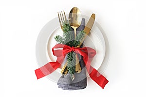 Traditional Christmas table place setting. Golden cutlery, linen napkin, green spruce branches, plate and red ribbon