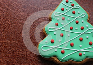 Traditional Christmas Tree Cookie Covered With Green Icing And Sweet Decor On Leather Surface Angle View