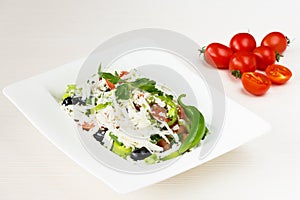 Traditional classic Shopska salad with tomatoes, peppers, cucumbers and cheese in white dish on white wooden table. Bulgarian cuis