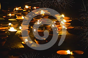 Traditional clay diya lamps lit during diwali celebration, fireworks in the background Happy Diwali - Lit diya lamp on street at