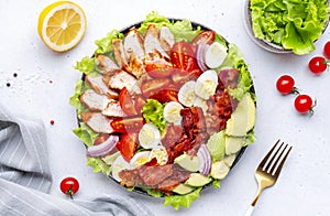 Traditional Cobb salad with chicken fillet, tomatoes, eggs, bacon, avocado and lettuce, gray table background, top view. American