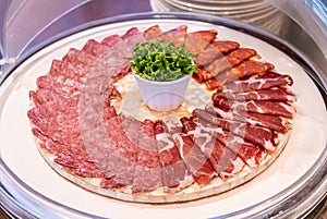 Traditional cold cuts with salami, sliced ham, sausage, prosciutto and bacon in a wooden platter