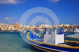 Traditional fishing boats, luzzu, anchored at Marsaxlokk, Malta. Blue sky and village background. Close up view.