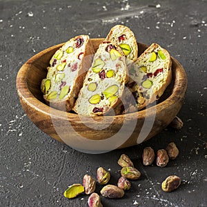 Traditional crispy Italian biscotti or cantuchini crackers with pistachios and dried cranberries in a bowl of olve wood