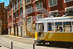 Traditional cute yellow vintage tram with woman inside on the street in Lisbon, Portugal in small alley with red buildings. Famous